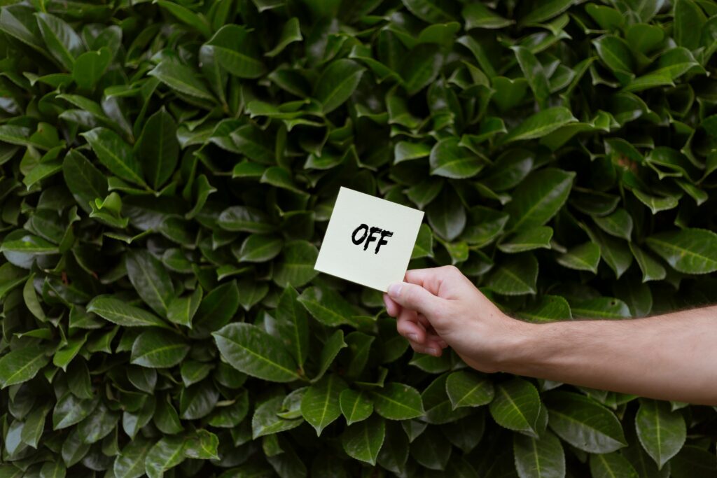A close-up of a hand holding a card with 'OFF' text in front of lush green leaves.